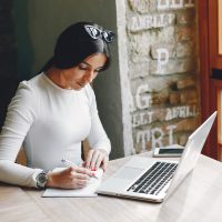 Beautiful girl with a laptop. Woman in a summer city. Lady sitting on the table