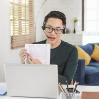 Smiling handsome asian businessman wear headphones working remotely from home. He is webinar video conference